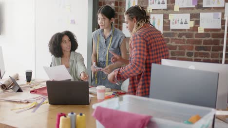 Busy-diverse-designers-using-laptop-and-discussing-work-in-fashion-design-studio-in-slow-motion