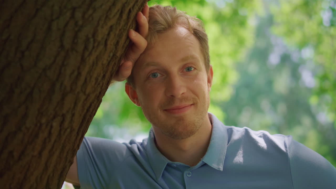 공원의 클로즈업에서 나무에 기울인 남자의 초상화. 카메라를 바라보는 예쁜 남자.