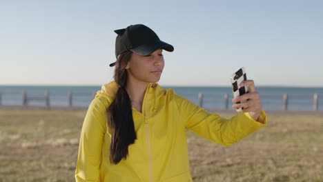 portrait of teenage girl smiling posing taking selfie photo using smartphone at seaside park