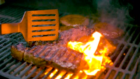 grilled meat or stake being moved around and thrown over with a spatula on a grill creating flames underneath it in slow motion