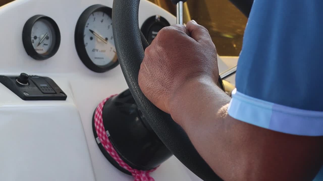 Detailed view of a person handling the boat's steering wheel and control panel.