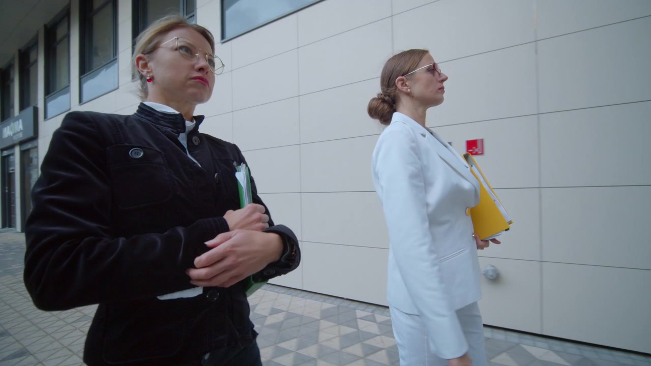 Ripresa in movimento di due donne d'affari in abito classico che camminano con passo fluido, tenendo cartelle di documenti
