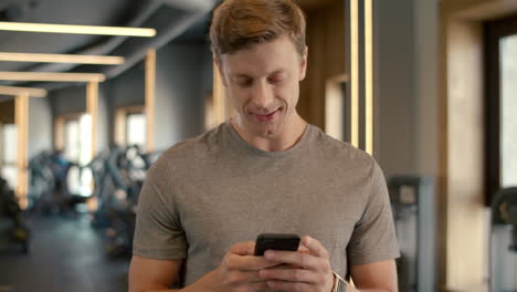 cheerful bodybuilder standing at gym. sportsman texting message in sport club