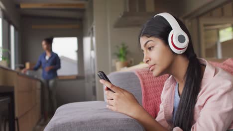 video de una mujer biracial feliz acostada en el sofá con auriculares y teléfono inteligente