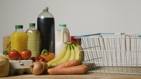 Studio-Shot-Of-Basic-Food-Items-Next-To-Supermarket-Wire-Shopping-Basket