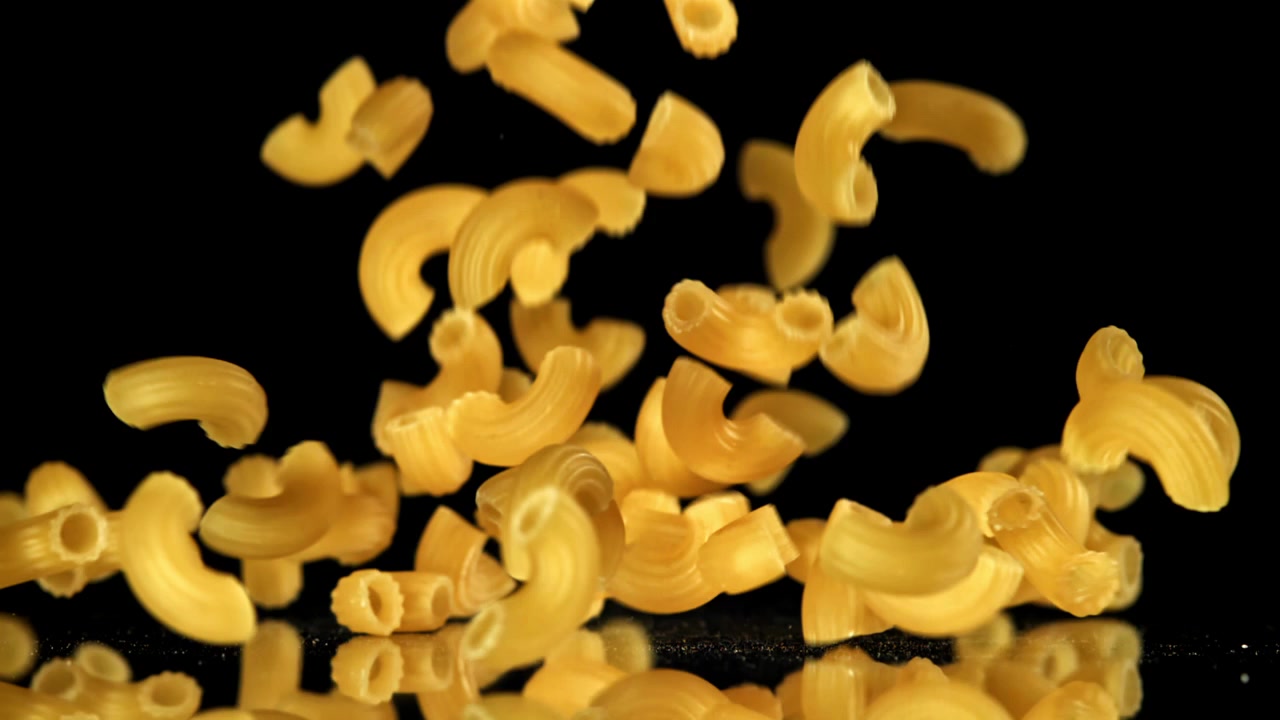 Pasta maccheroni secca che cade al rallentatore su sfondo nero.