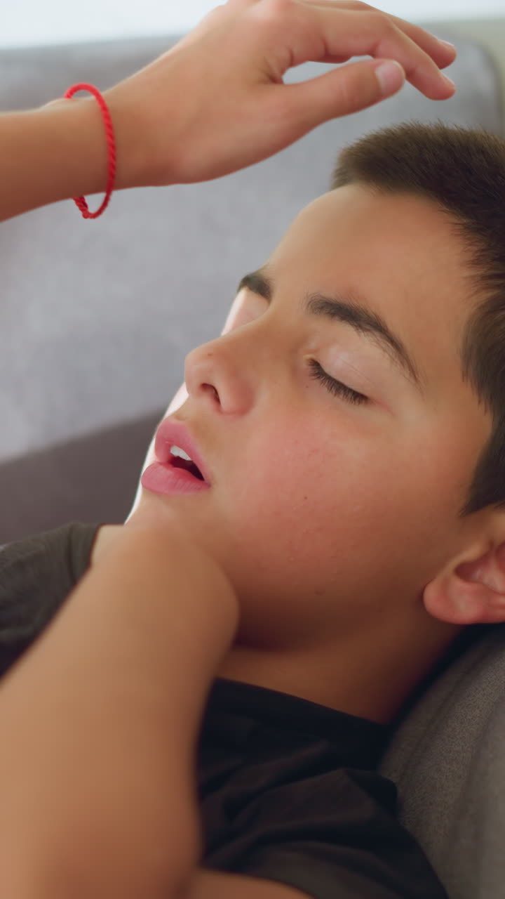 Partial view of person handing thermometer to sick boy covered with blanket, boy checking temperature with thermometer, concerned expression, indoor setting with soft lighting