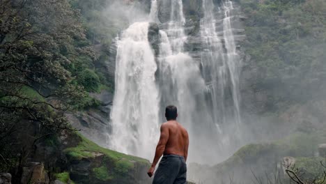 A man enjoys the natural beauty of Bomburu Falls, one of the widest waterfalls in Sri Lanka, located in the lush mountainous region of Nuwara Eliya.