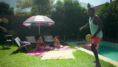 diverse friends enjoying sunny day by pool, playing catch and relaxing on towels