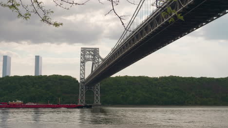 red barge makes its way under the gw bridge as it head up the hudson river and past upper manhattan