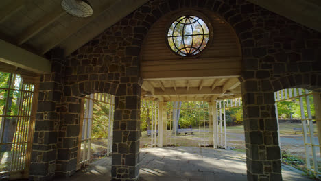 a pan tilt shot of an intricate gazebo, starting with a circular window and revealing colorful trees and a calm lake in the exterior