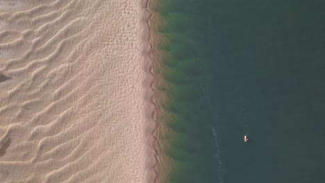 Un-Kayak-Solitario-Remando-A-Lo-Largo-De-La-Impresionante-Costa-De-Arena-Dorada,-De-Arriba-Hacia-Abajo