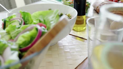 Bowl-of-salad,-olive-oil-and-slices-of-bread-on-table