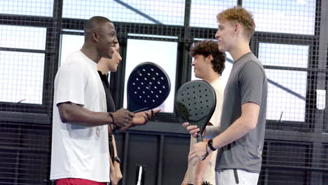 diverse friends enjoying padel tennis match, holding rackets and smiling, on indoor court