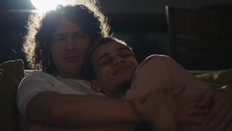 lockdown of young gay couple in embrace on couch in living room, having rest and watching movie