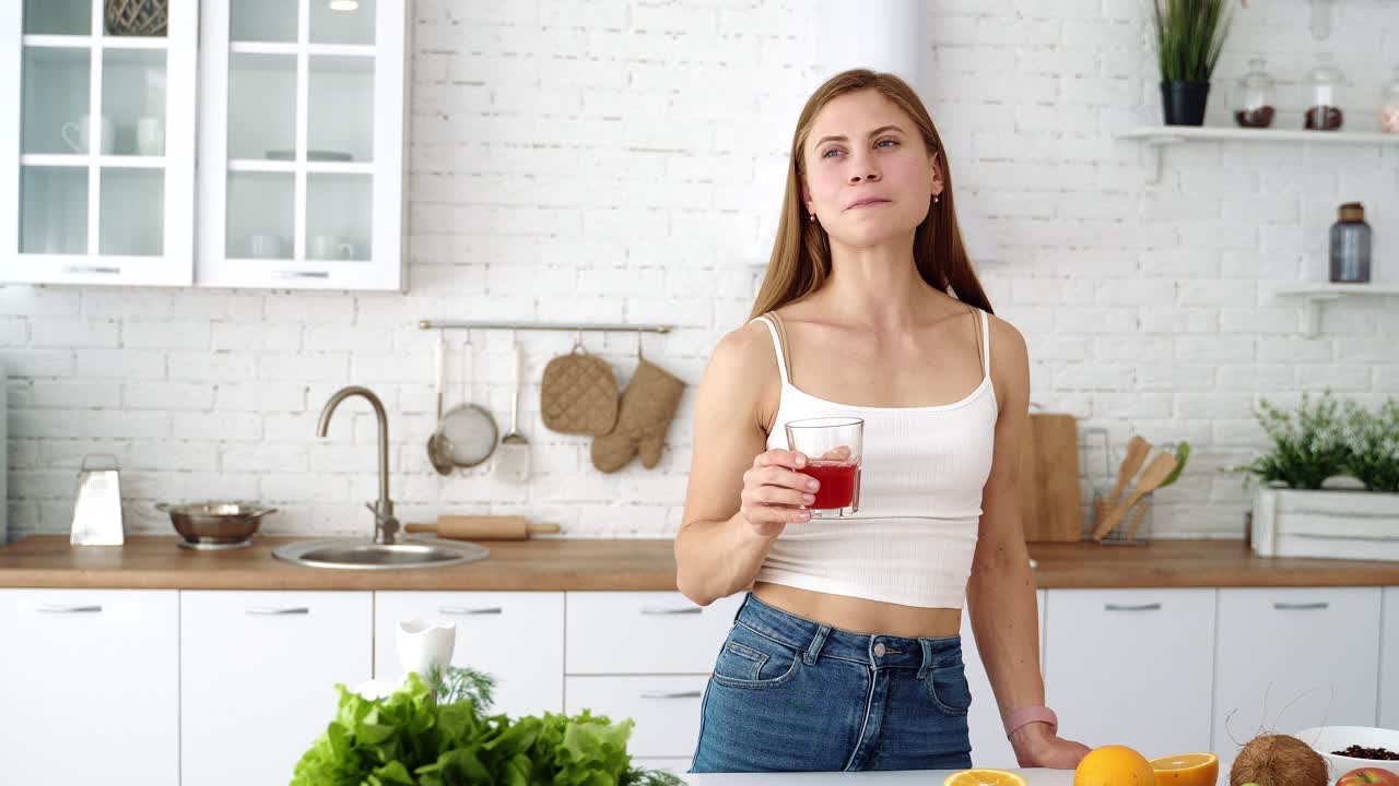 La ragazza in cucina beve succo di frutta fresco. Tavolo con frutta e verdura per una dieta sana.