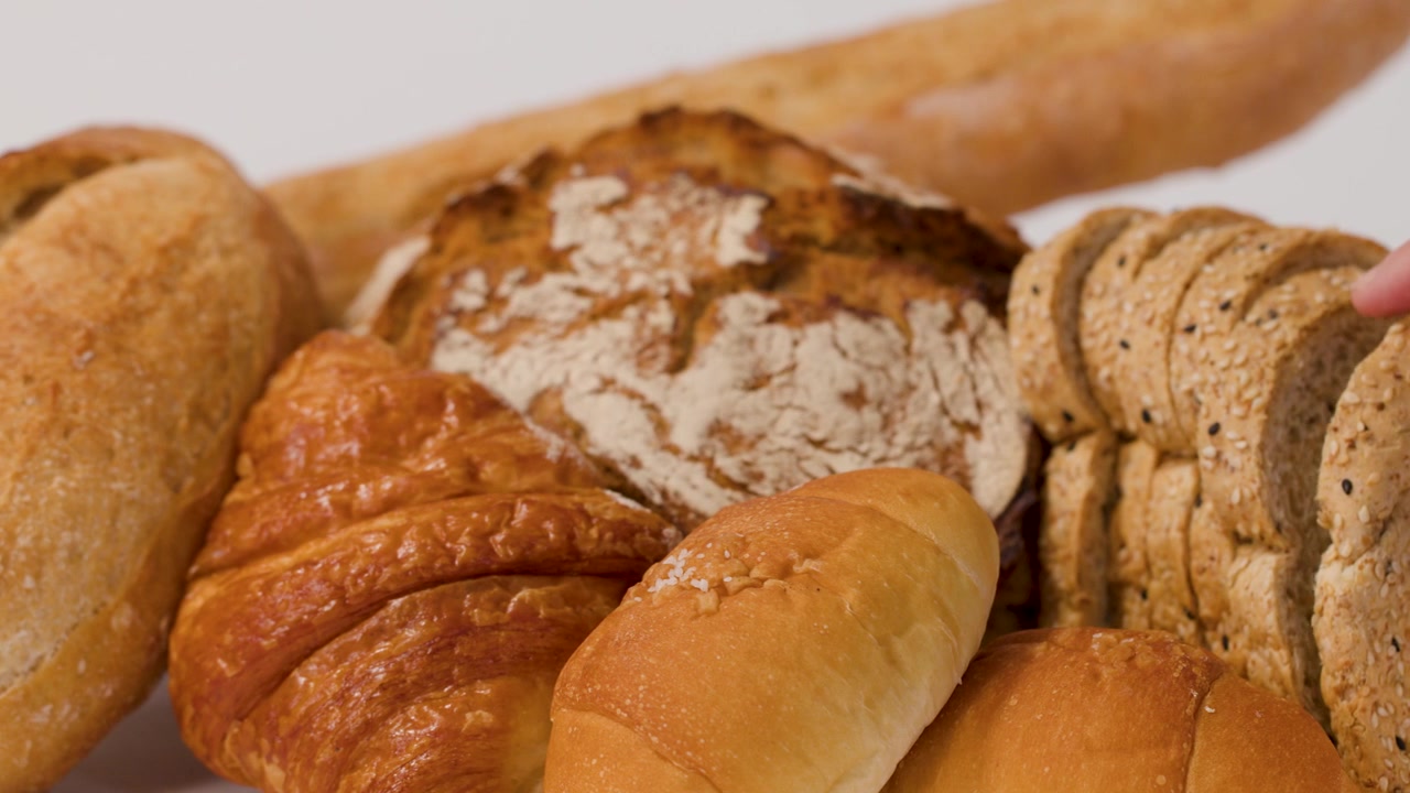 Close-up shot of hands selecting sliced multigrain bread from a variety of fresh artisan pastries.