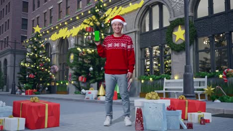 hombre sosteniendo un teléfono inteligente con pantalla verde en un entorno navideño