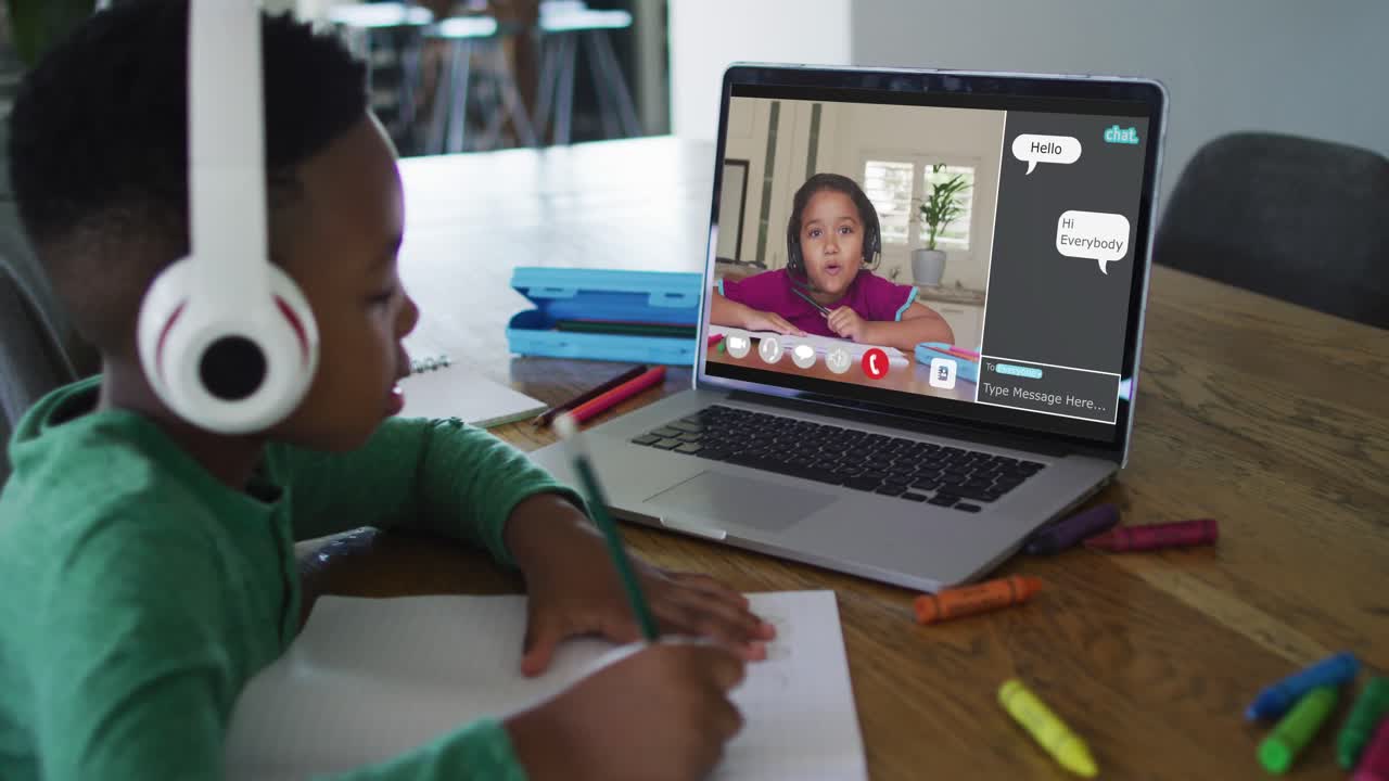Schoolboy using laptop for online lesson at home, with schoolgirl and web chat on screen