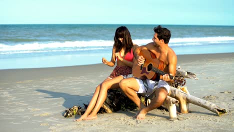 multi ethnic couple playing guitar on beach vacation