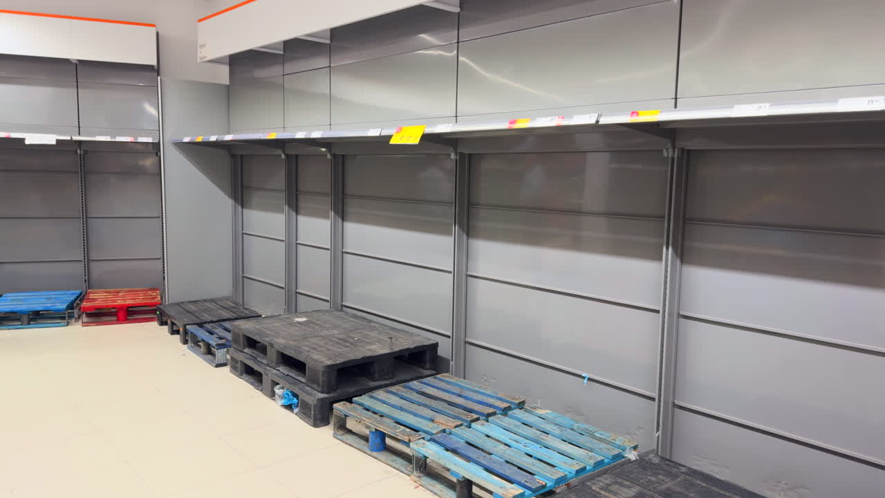 Empty shelves in a supermarket, surrounded by colorful pallets on the floor, highlighting the current food scarcity crisis.