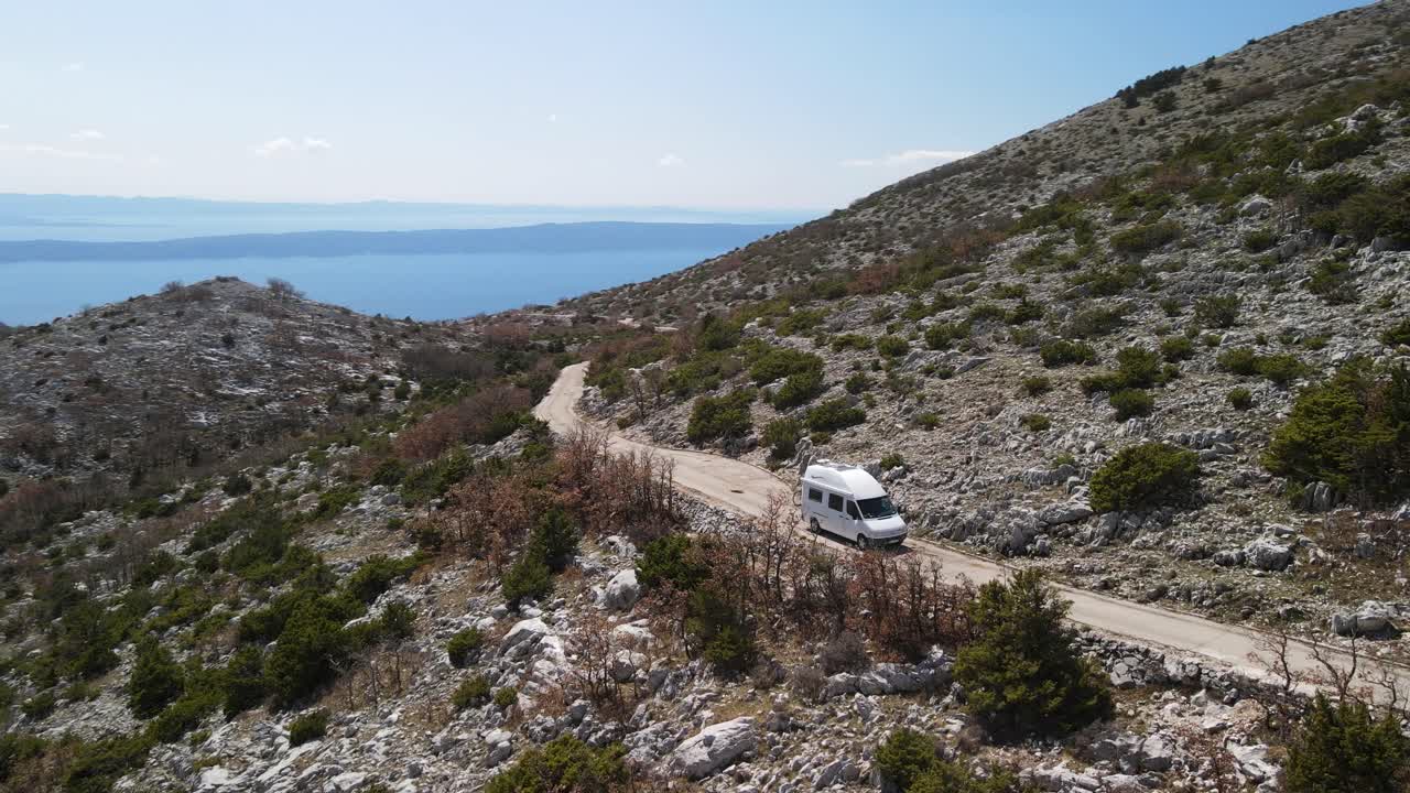 autocaravana fuera de la red en un camino de grava de montaña vacío contra el océano azul