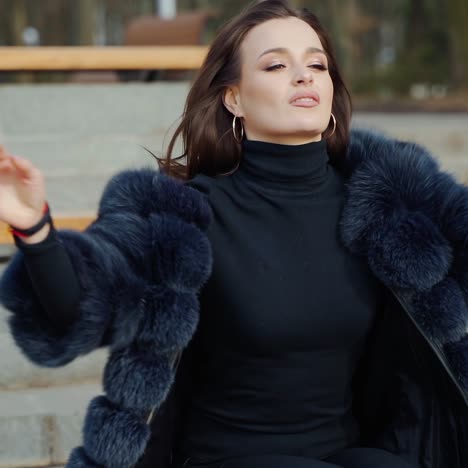sexy brunette woman posing wearing dark fur coat looking to tha camera with hands near face. fashion video.