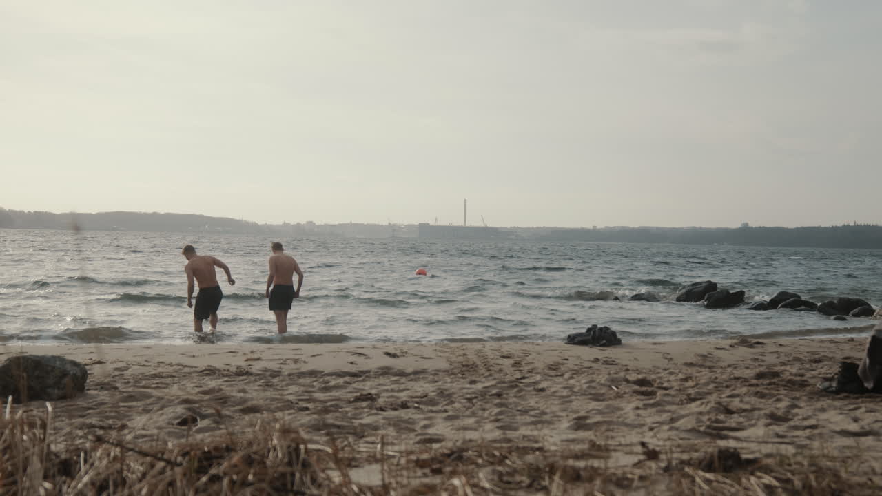 Two young males walking from the beach in the cold water in January