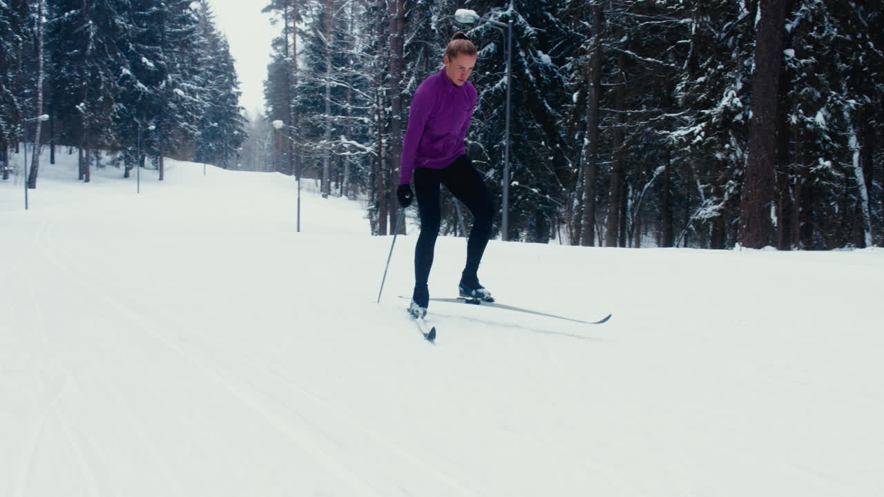 젊은 백인 여성 운동 선수가 경치 좋은 숲길에서 크로스컨트리 스키를 연습하고 있습니다.