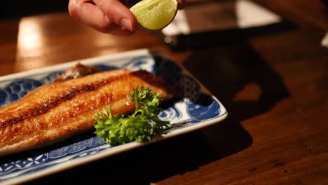 hand squeezing lemon over grilled fish dish