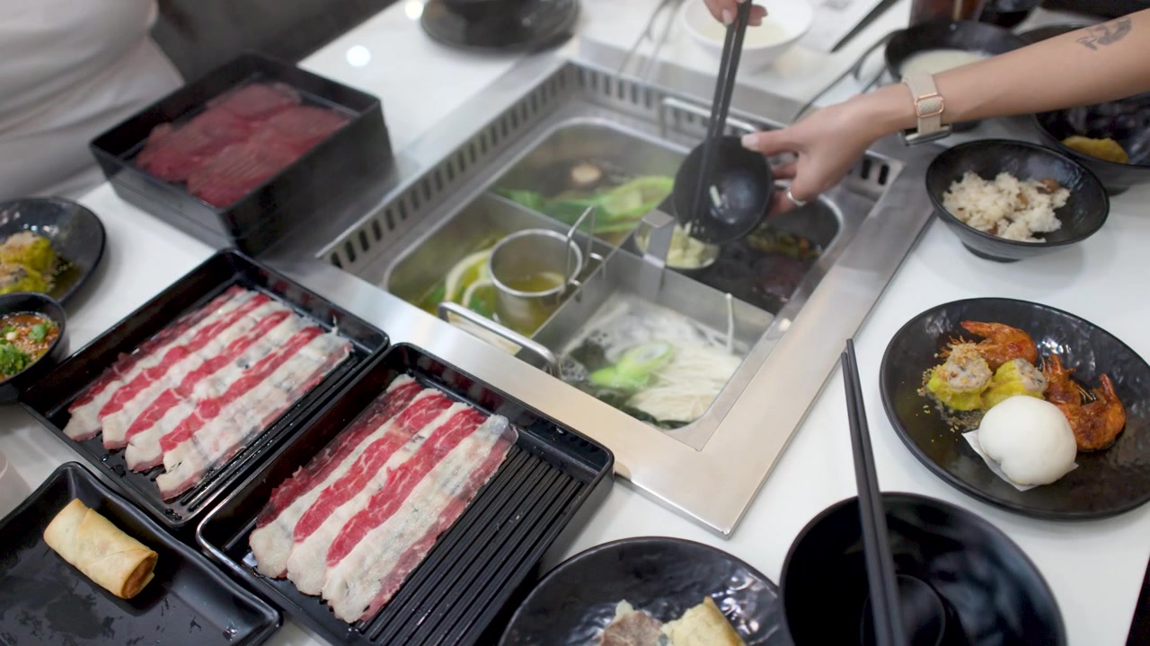 Tomada de ângulo alto de clientes usando conchas em uma panela de sopa shabu shabu fervente.