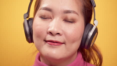 밝은 노란색 배경에서 편안하게 헤드폰으로 음악을 듣기 위해 디지털 태블릿을 사용하는 젊은 아시아 여성