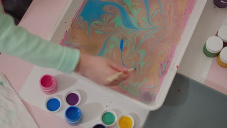 una pequeña artista dibuja un patrón abstracto en agua colorida