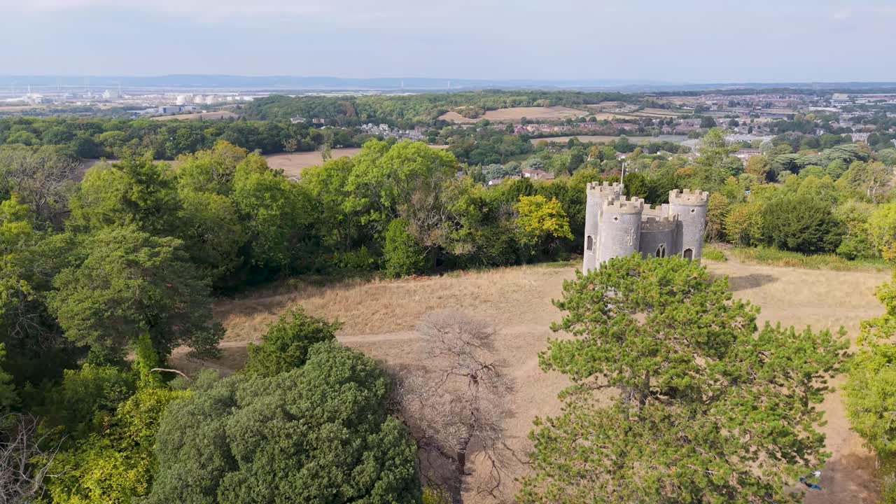 Aerial drone flies over Blaise Castle, Henbury, Bristol. Starting behind trees, it rises to reveal the historic folly before flying overhead, showing surrounding woodland and grassy parkland