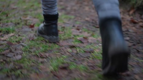 Spaziergang-Mit-Schwarzen-Stiefeln-Auf-Waldweg-Mit-Braunen-Blättern,-Nahaufnahme