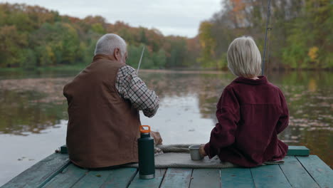 grandfather and grandson fishing on a lake pier in autumn
