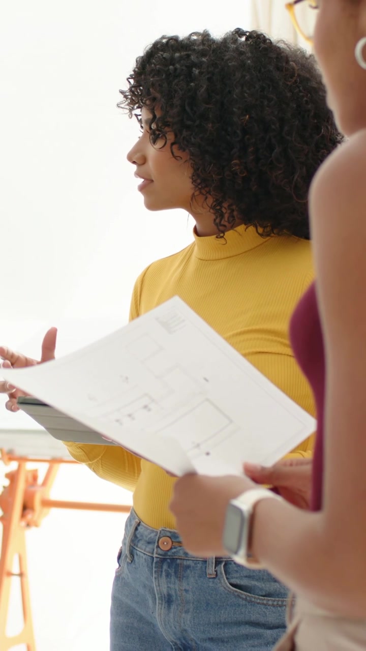 Vertical video: Seeing plan, woman in yellow top talking and pointing at tablet in studio, watch