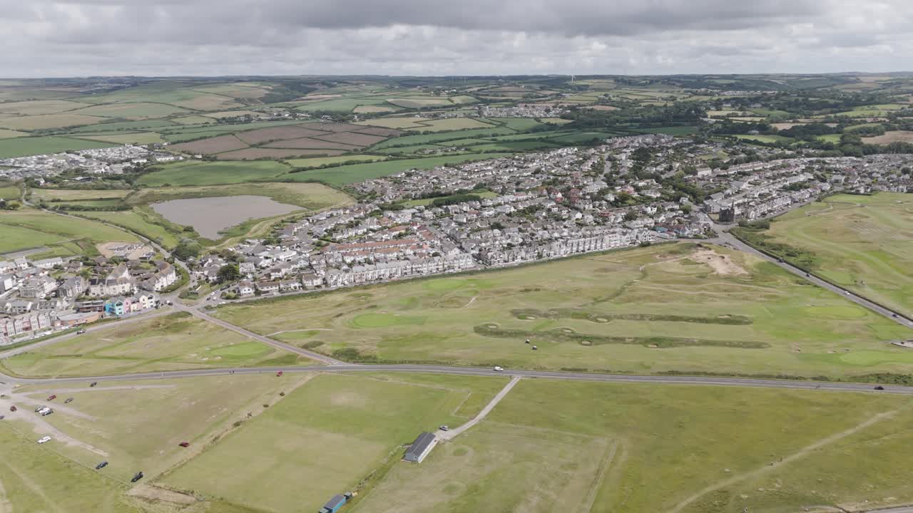 Veduta aerea di una città costiera con aree residenziali, campo da golf e campi verdi sotto cieli nuvolosi