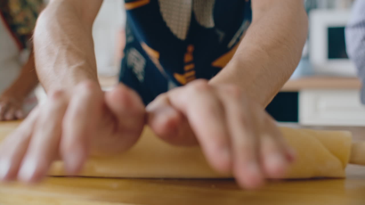 Hands of Man Flattening Dough with Wooden Rolling Pin on Kitchen Counter