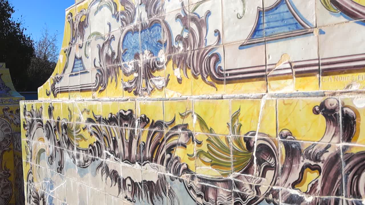 Primer plano de coloridos azulejos históricos con desgaste y grietas visibles en una pared de un jardín real bajo la luz del sol brillante