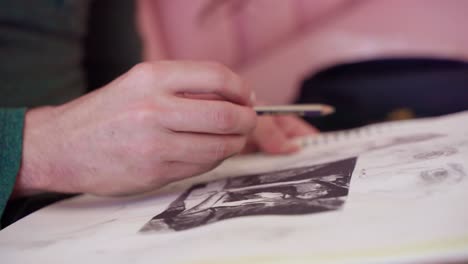 extreme close up profile shot of artist's hand drawing picture on sketch pad with graphite pencil