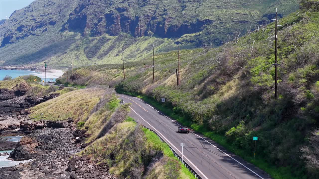 Convertible on Farrington Highway at the base of Waianae mountains, aerial