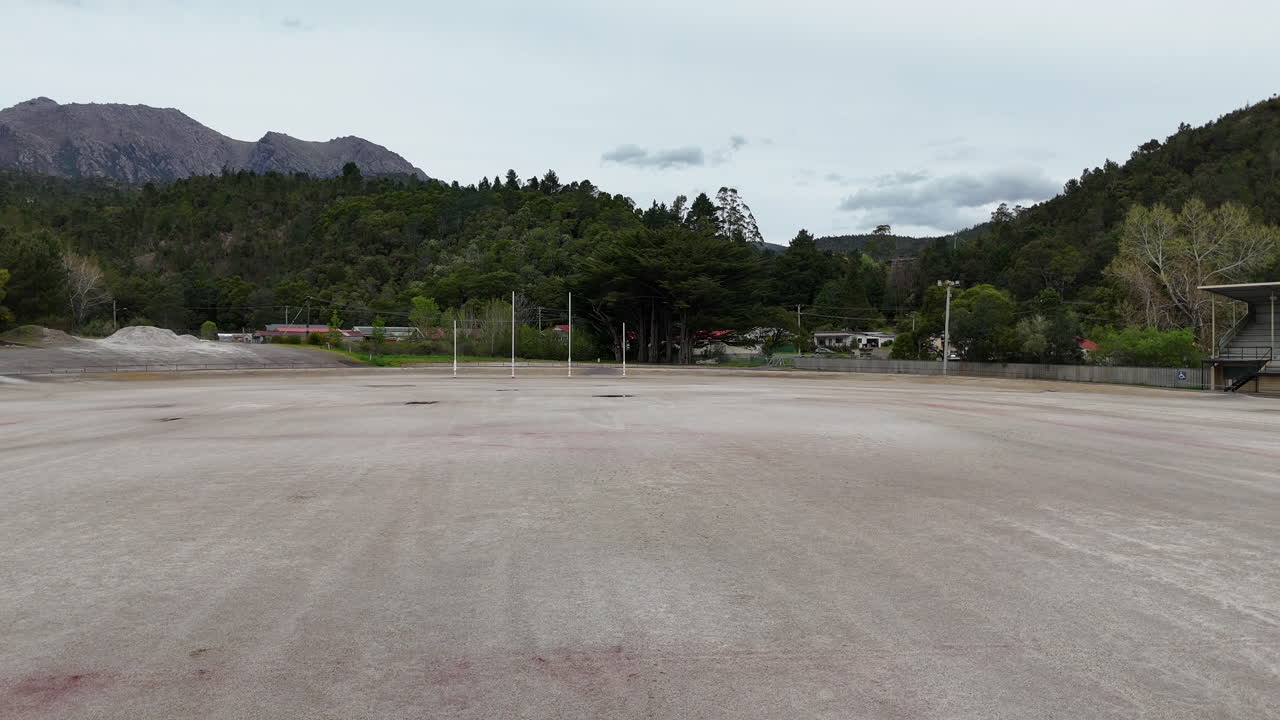 This Australian rules football field in Queenstown Tasmania features a unique sand base. Surrounded by mountains and greenery, the setting offers a perfect backdrop for local sports activities.