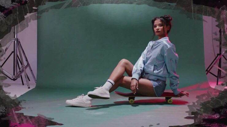 Video verticale: Modella in posa su skateboard rosso in movimento in un set verde, che indossa una giacca blu per le riprese