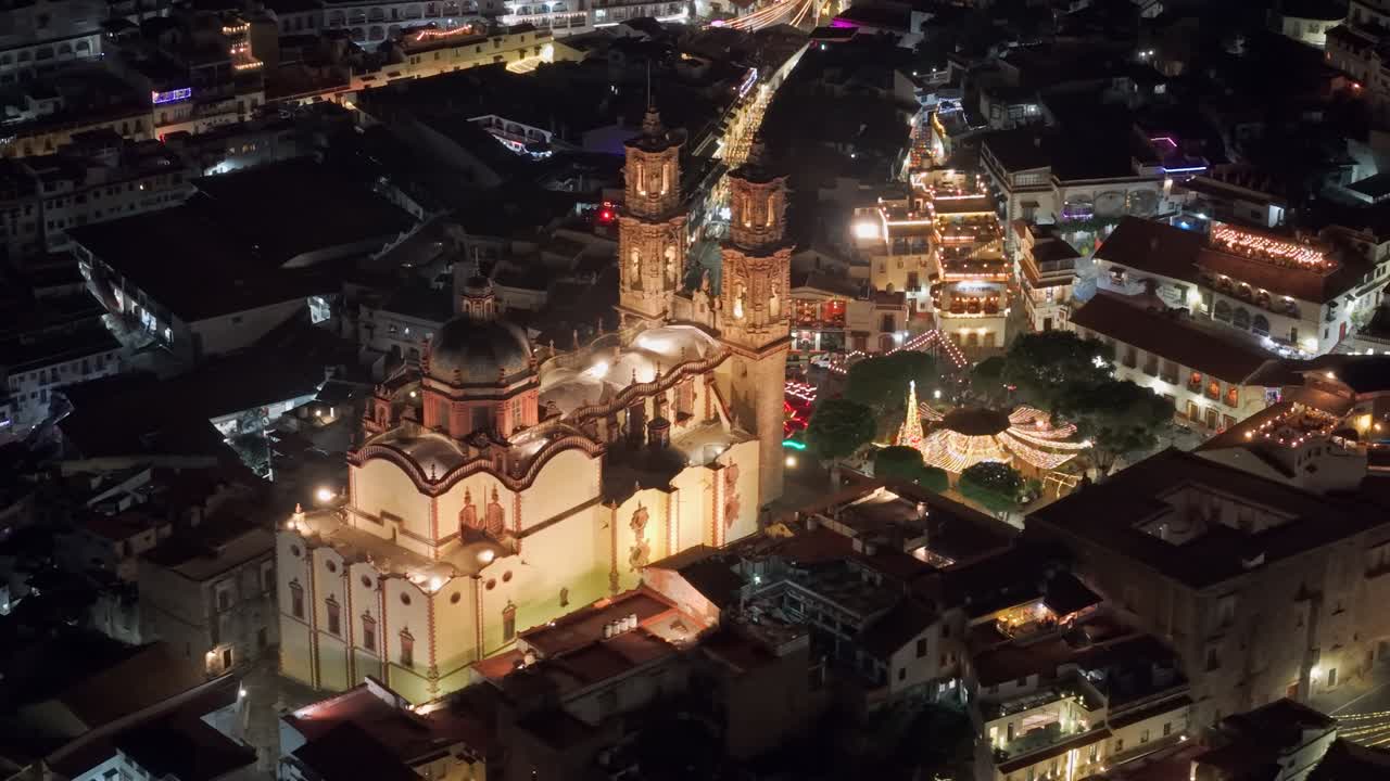 Vista aerea teleobiettivo isolata del tempio di Santa Prisca illuminato di notte con luci nella piazza e case coloniali bianche tutt'intorno, Taxco, Guerrero, Messico