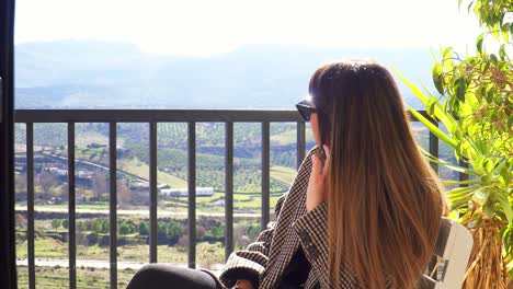 caucasian girl with sunglasses, straight hair and red lips sitting and touching her hair against the background of some fields and the horizon