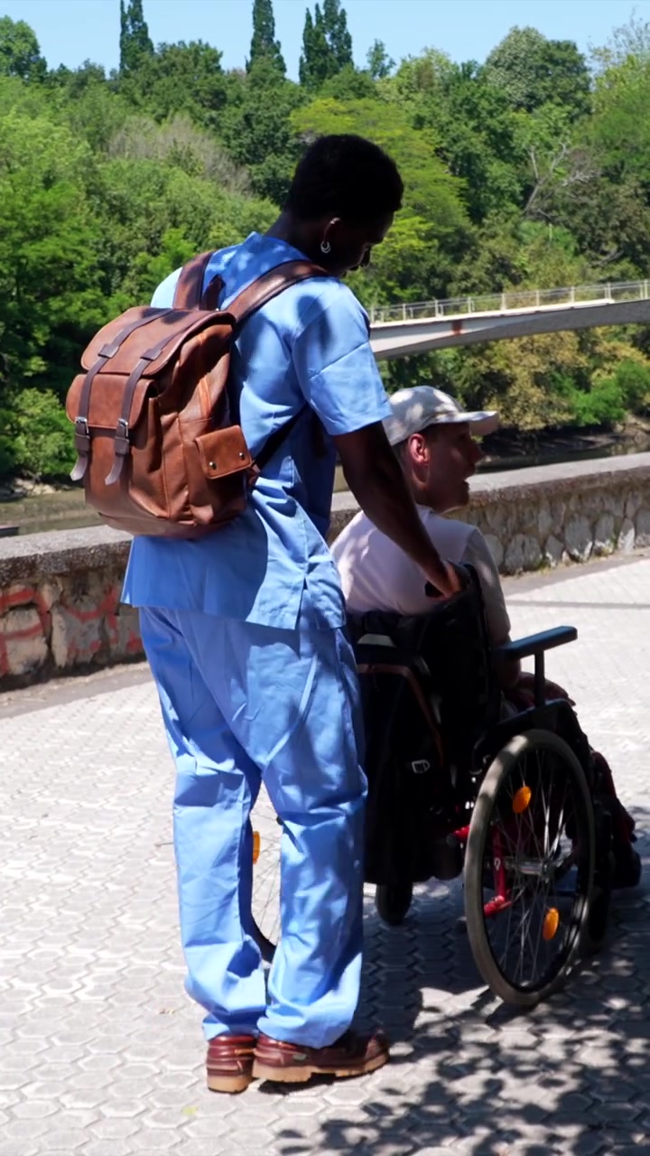 Assistente che spinge un paziente anziano su sedia a rotelle all'aperto