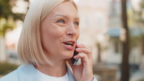 happy mature caucasian businesswoman lady smiling laughs while talking on smartphone on city street