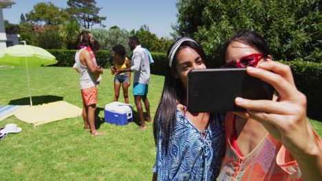 two mixed race female friends taking selfie at a pool party