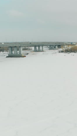 boundless white frozen river surface covered with snow and ice under high bridge surrounded by forests bird eye view